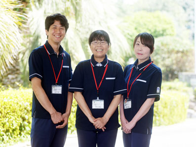 介護施設のスタッフ3名が制服を着て笑顔で並ぶ写真。屋外での記念撮影。